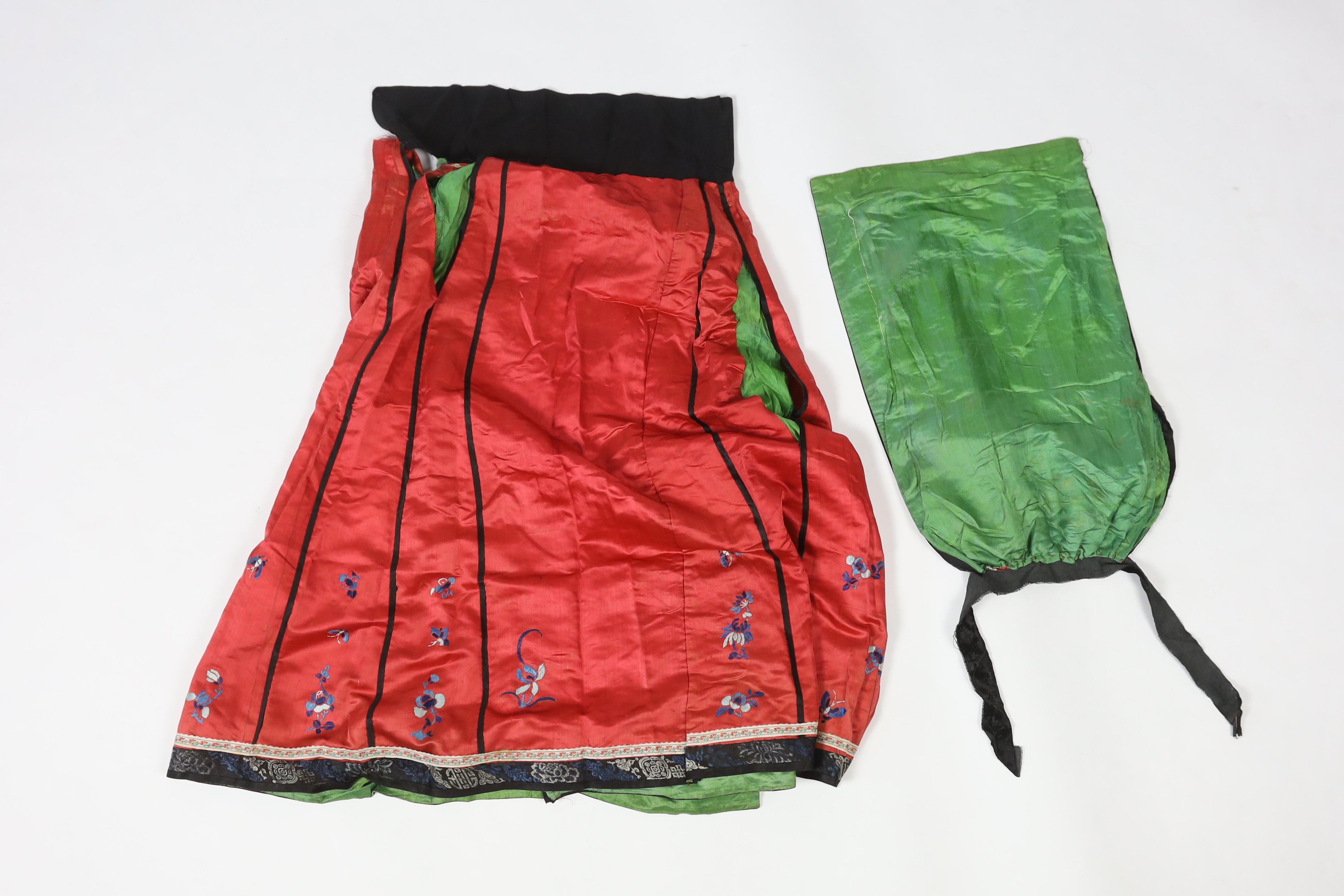 A Chinese red silk skirt, embroidered with a blue silk panel of Chinese knotting flowers and auspicious symbols, the bottom of the skirt with spot motifs bordered with embroidered braiding and ribbon, the slant is lined